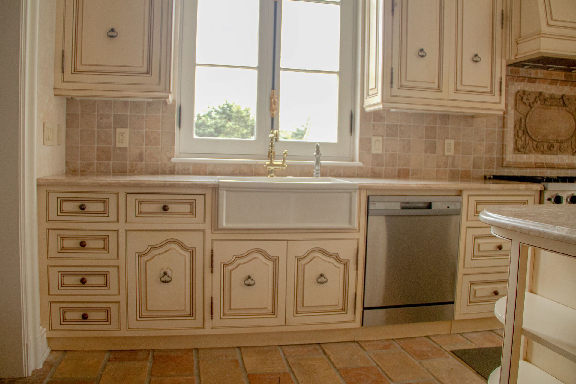 Cream-colored kitchen cabinets with distressed finish, farmhouse sink, dishwasher, and tile backsplash.