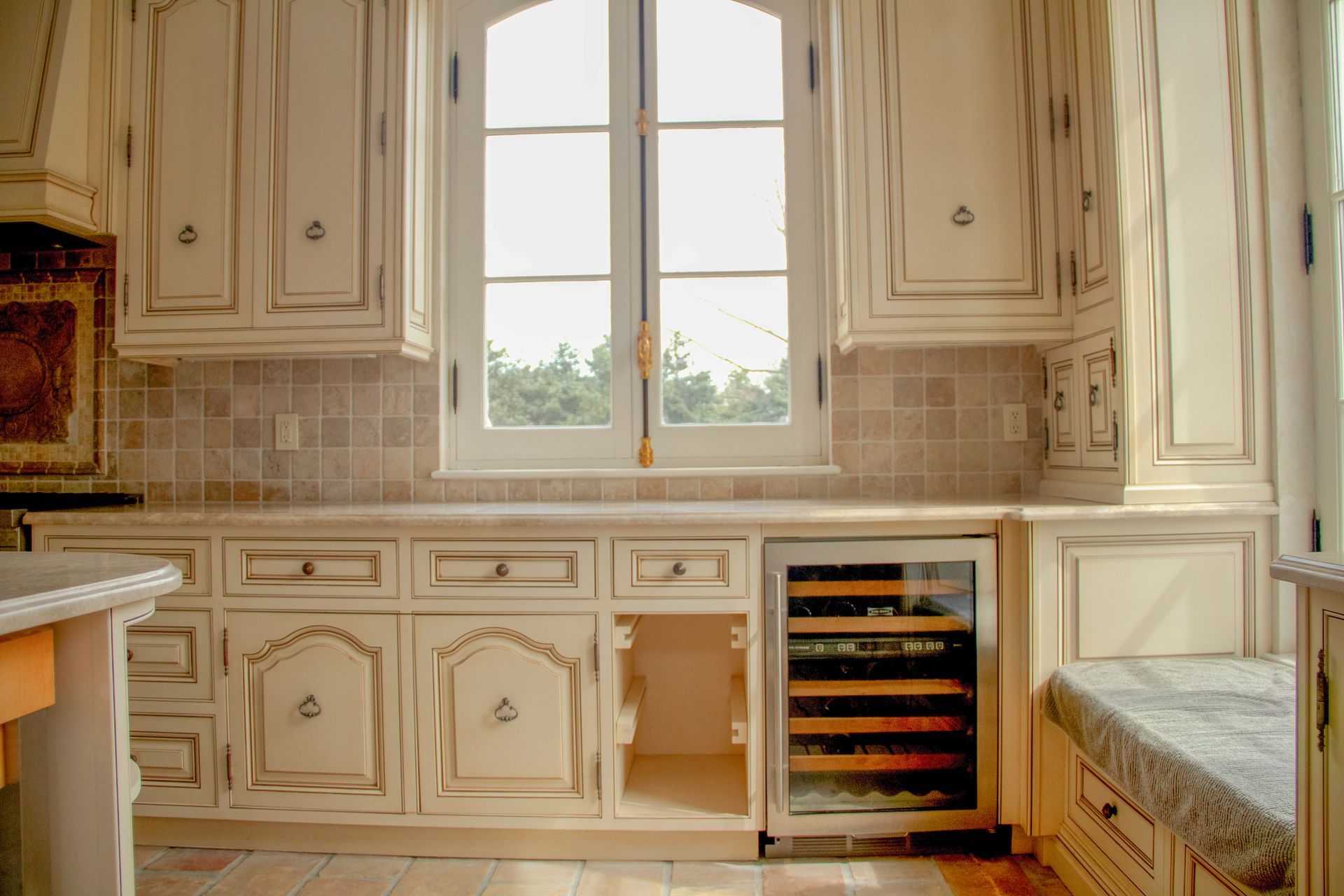 Cream-colored distressed kitchen cabinets with a window, tile backsplash, and built-in wine fridge.