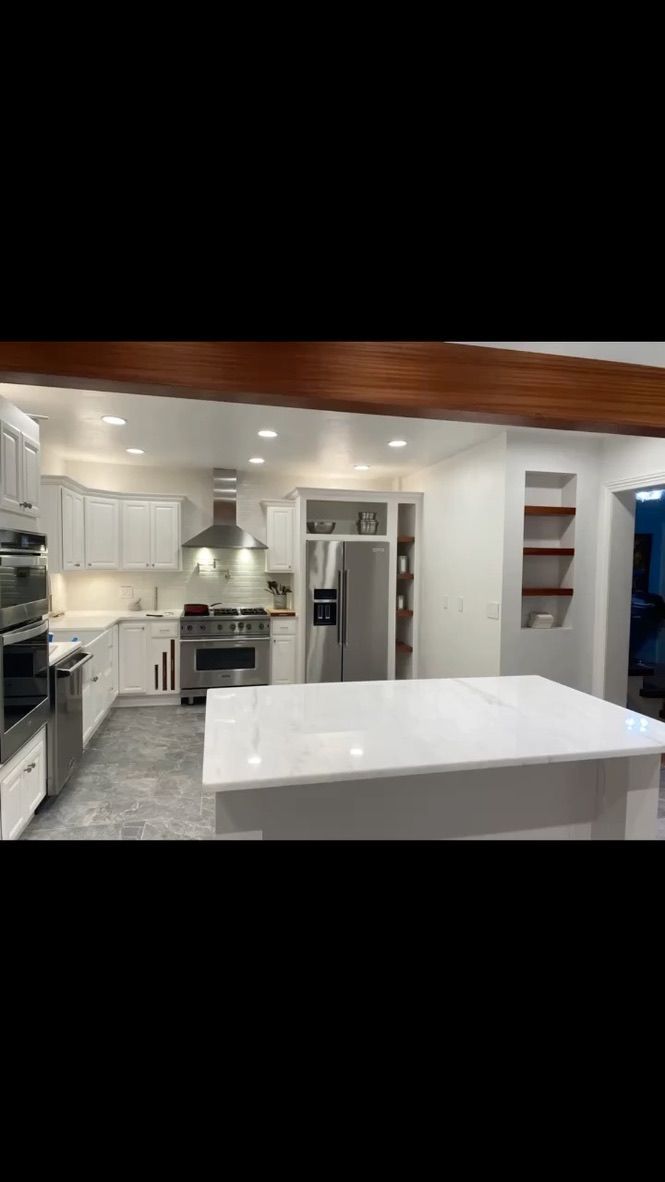Modern kitchen with white cabinets, stone-topped island, stainless steel appliances, and a rustic wooden ceiling beam.
