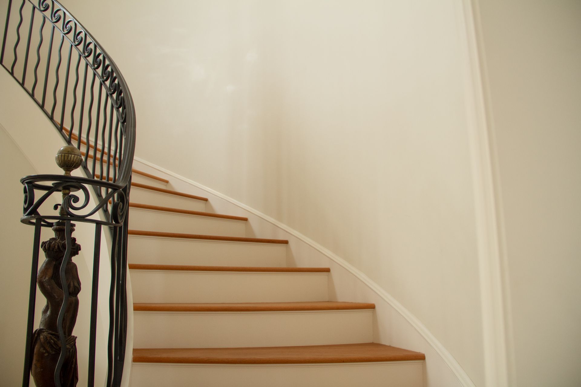 Curving staircase with wooden steps, white risers, and ornate black railing against a cream-colored wall.