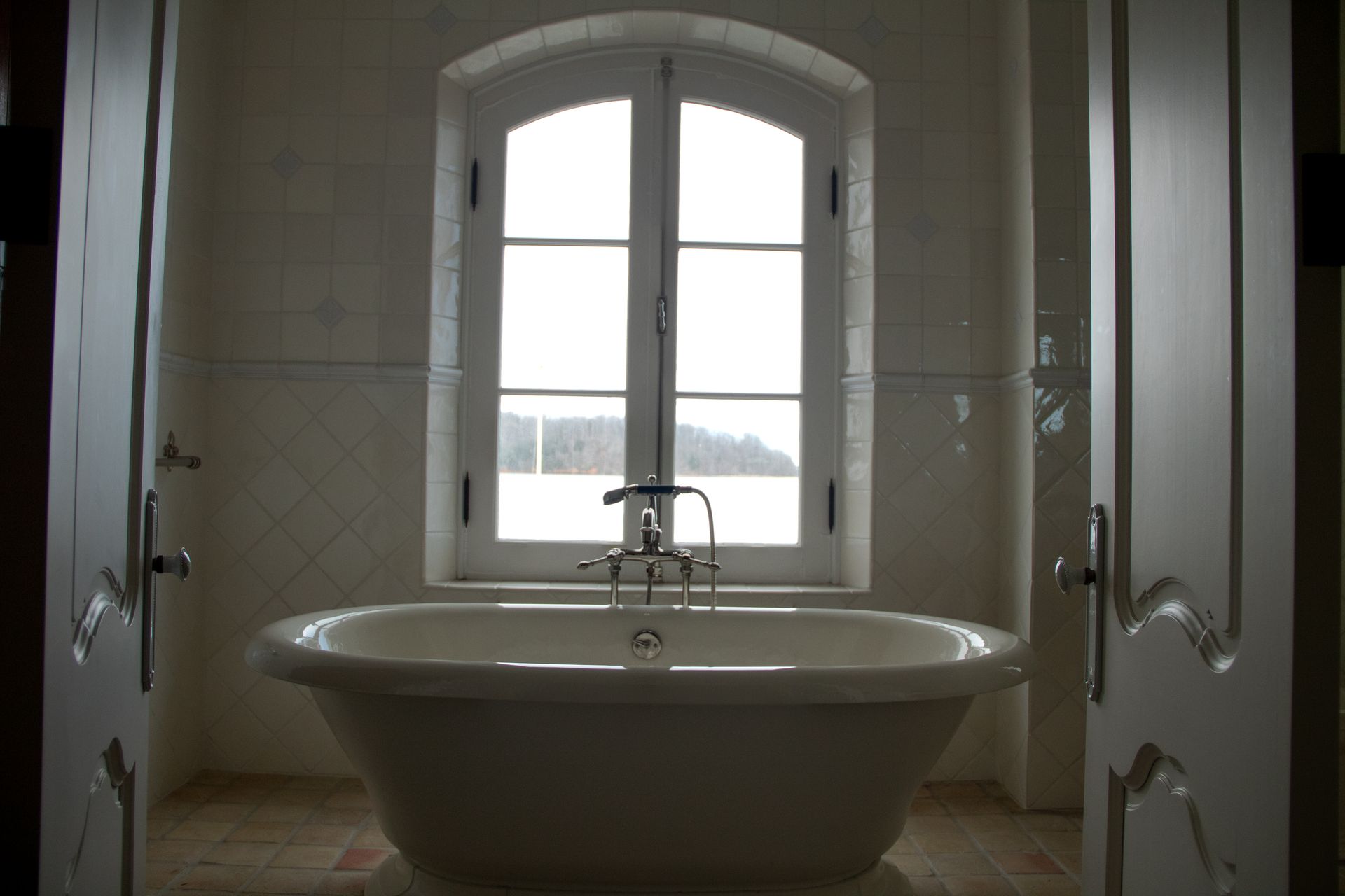 Bathroom with a white clawfoot bathtub centered under a window. White doors are on each side.