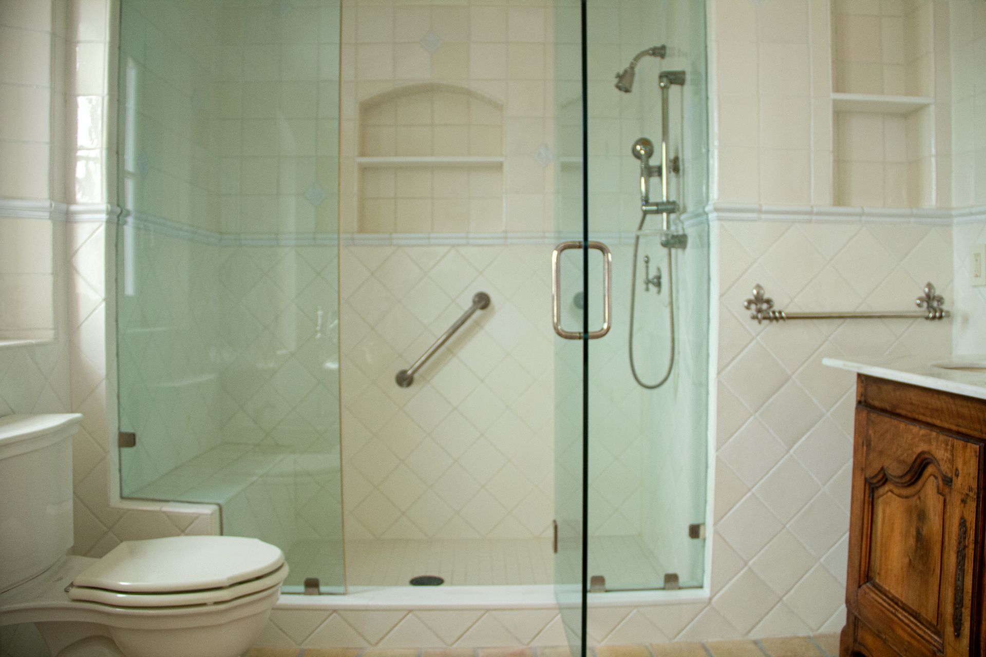 Bathroom with glass shower, toilet, and wooden vanity. Features include a grab bar and built-in shelves.