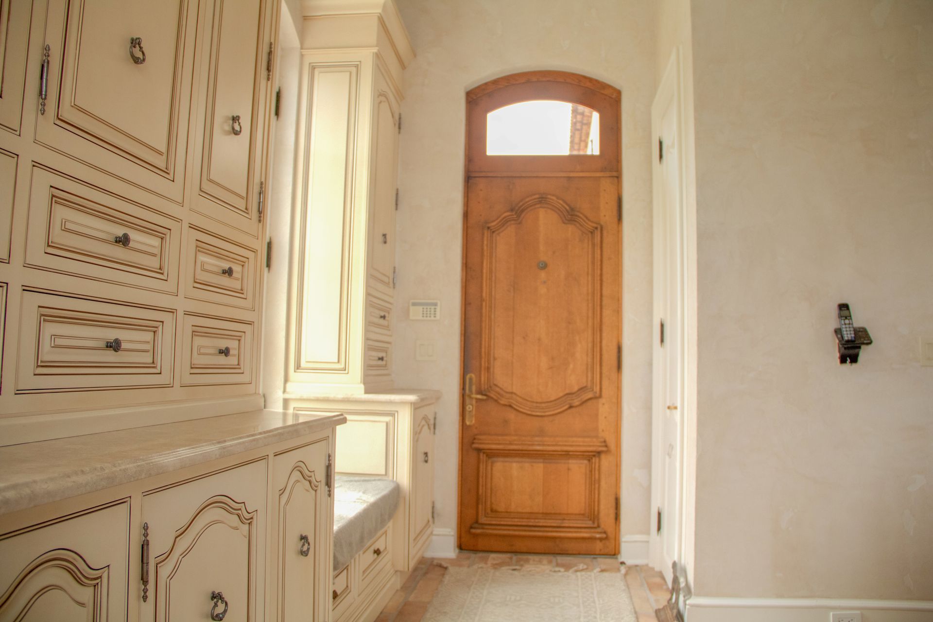 Wooden front door with arched top, surrounded by off-white cabinets and a window seat.