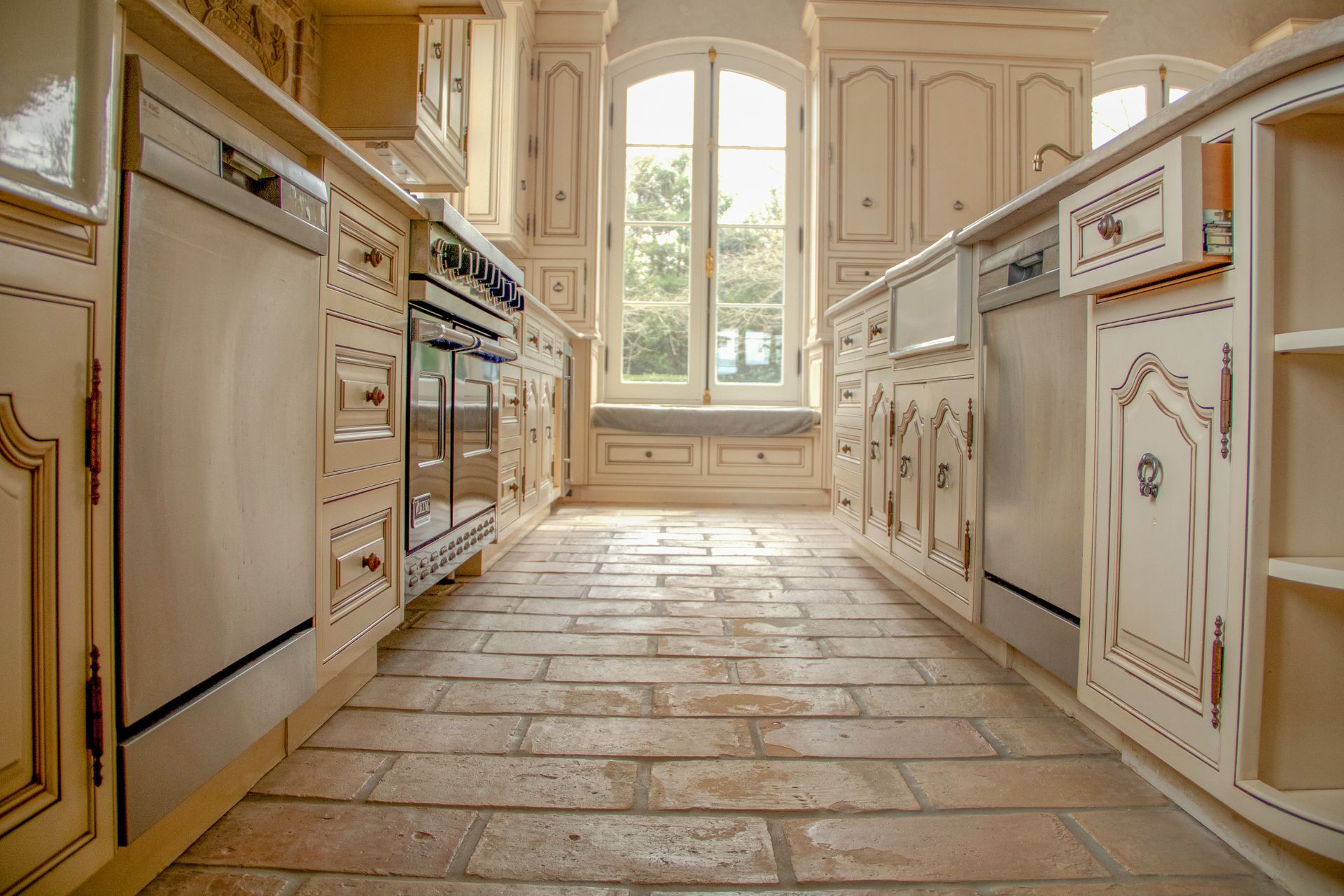 Kitchen with light cabinets, brick floor, and a window.