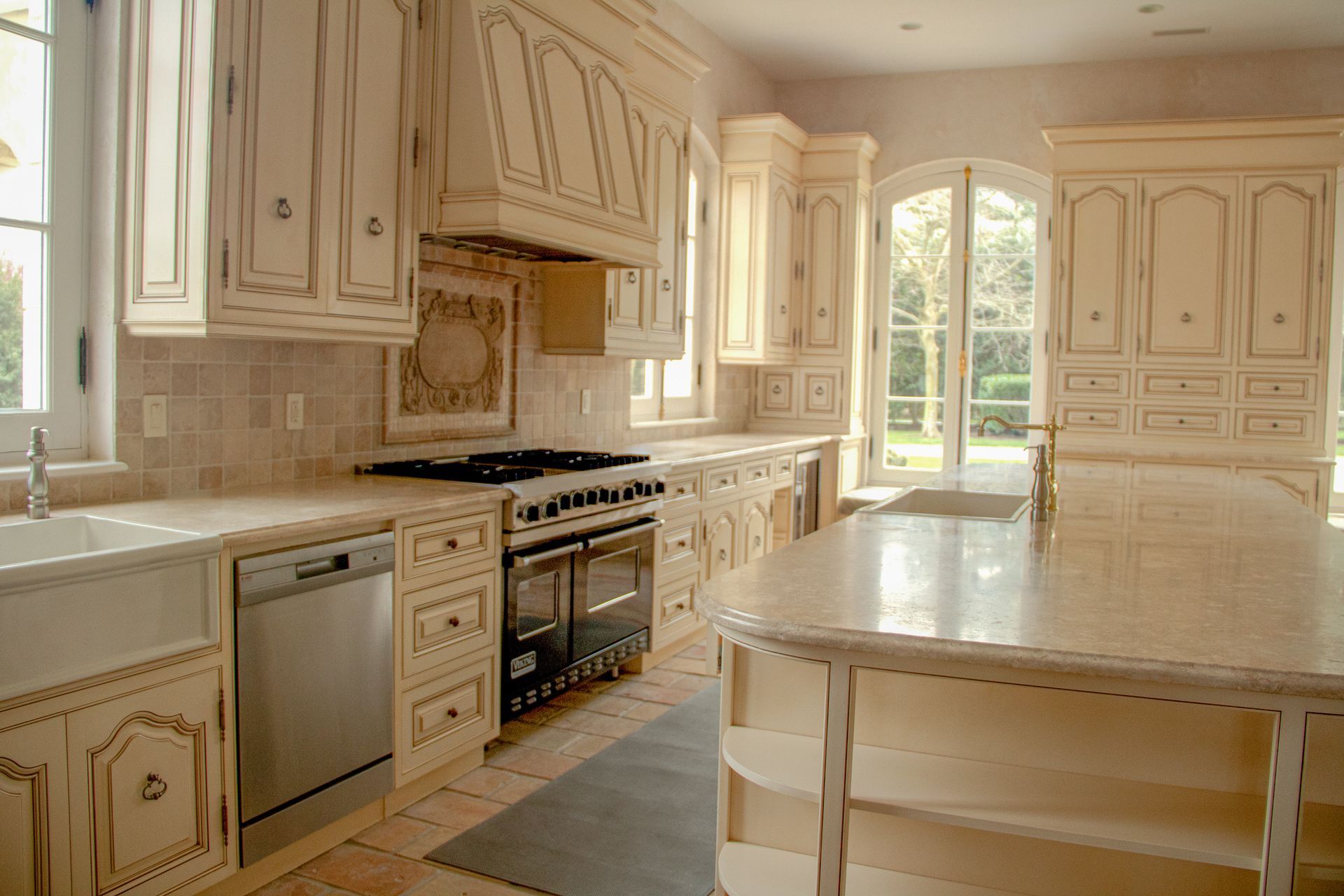 Cream-colored kitchen with ornate cabinets, black stovetop, stainless steel appliances, and large window.