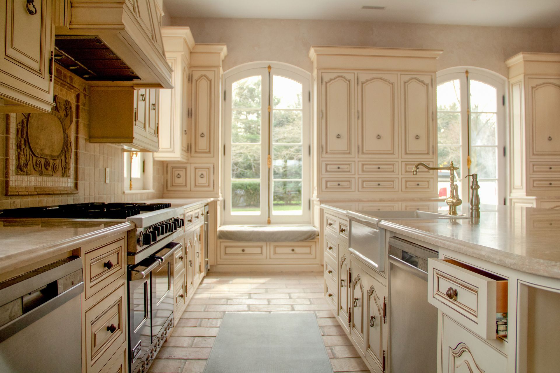 Cream-colored kitchen with arched windows, light wood cabinets, and brick floor.