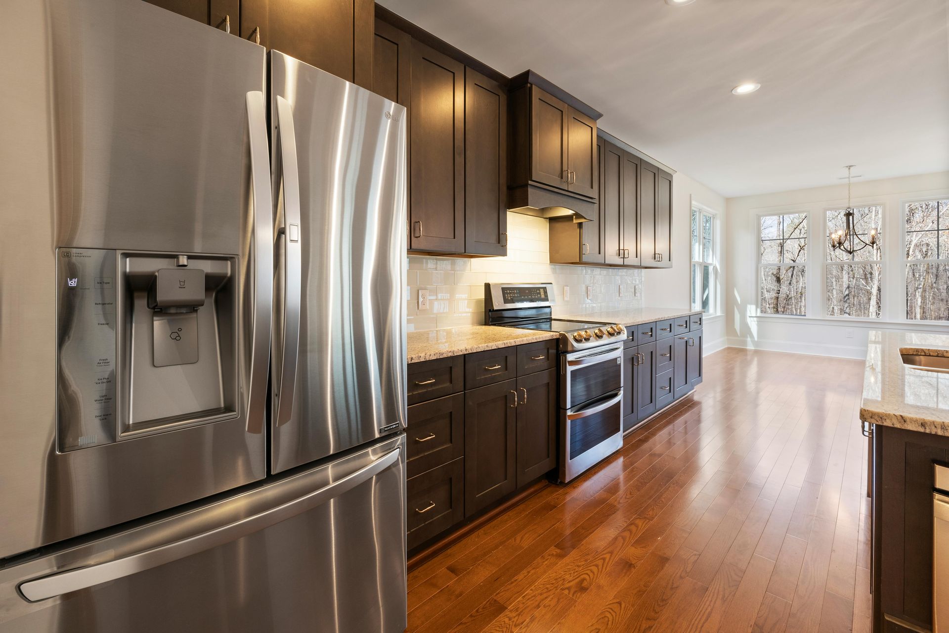 A modern kitchen with dark brown cabinets, stainless steel appliances, granite countertops, and hardwood floors.