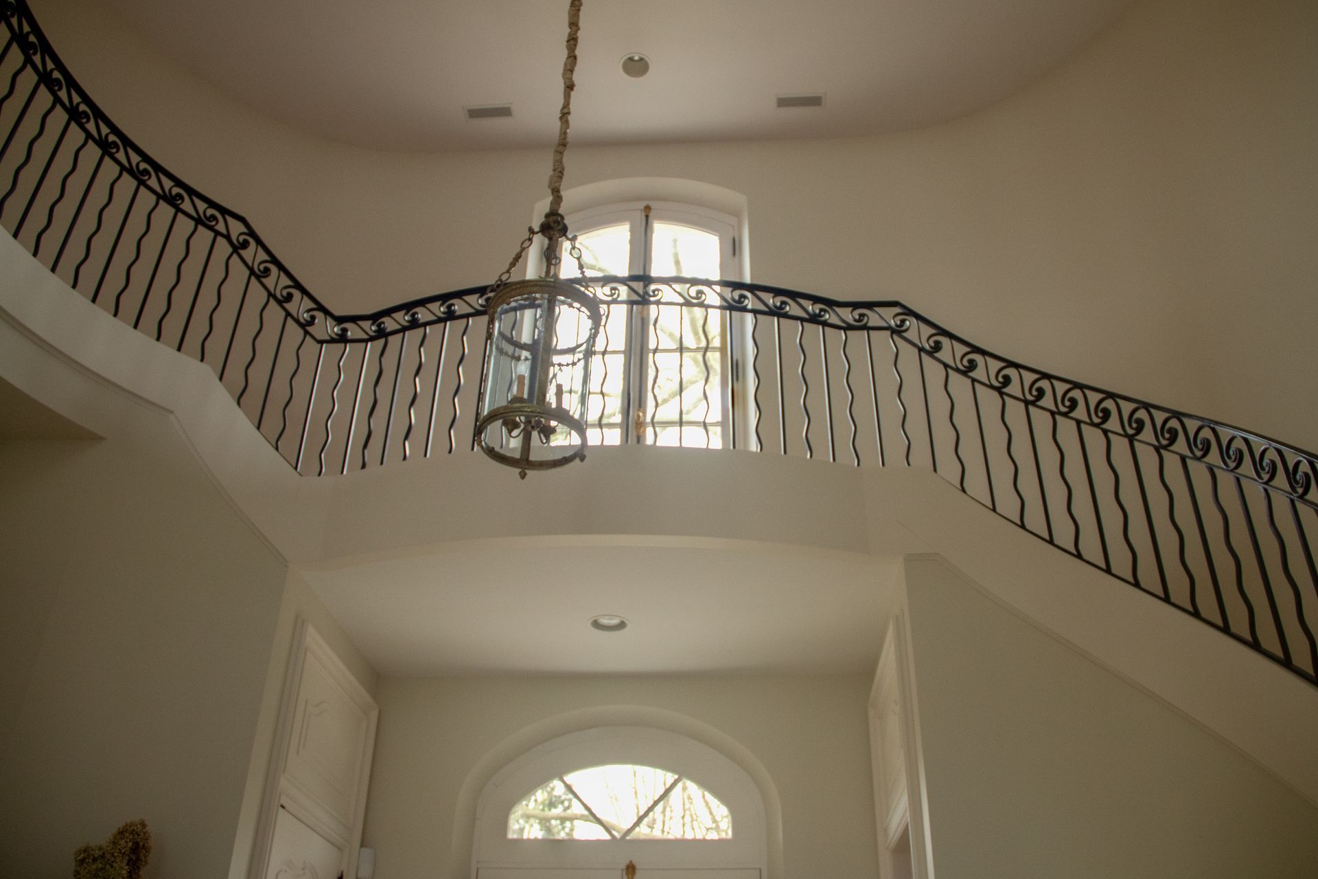 A grand foyer with a curved staircase, ornate black railing, and a hanging chandelier.