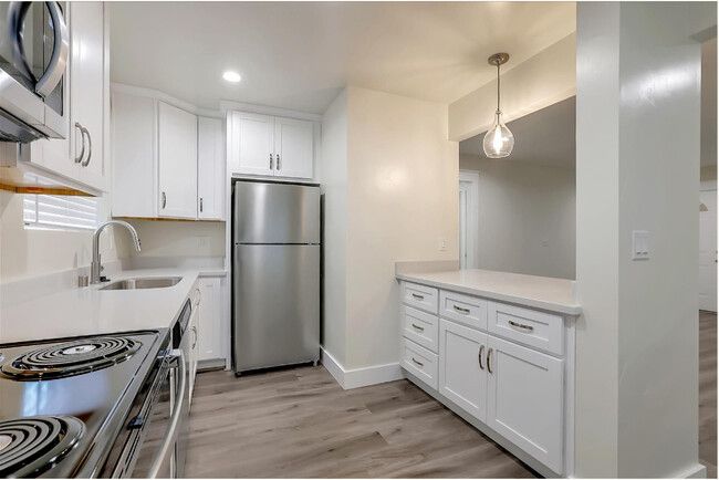 A kitchen with white cabinets , a stove , a refrigerator , and a microwave.