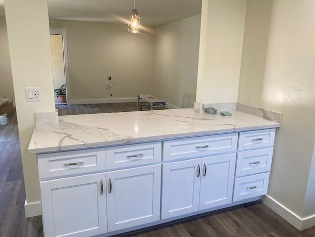 A kitchen with white cabinets and marble counter tops.