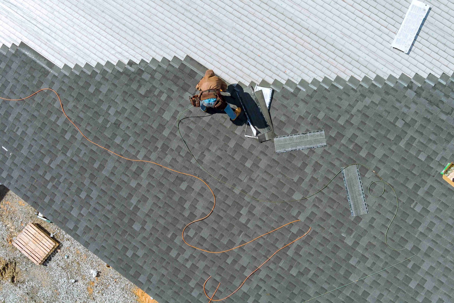 Roofer installs shingles on a residential roof with tools and safety lines.