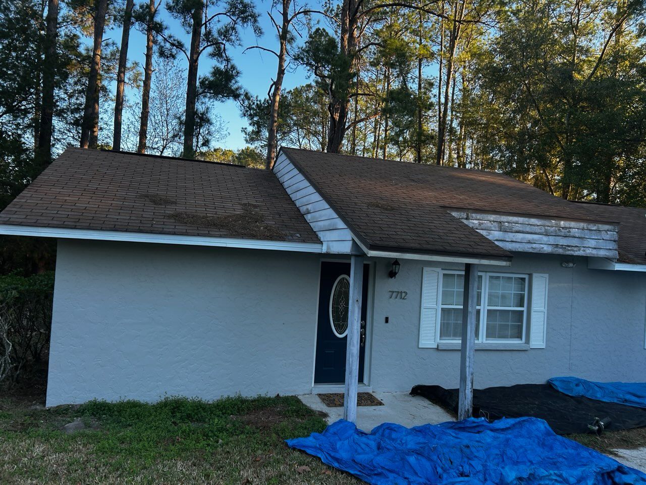 Exterior of a light blue house with a brown roof and a blue tarp on the ground.