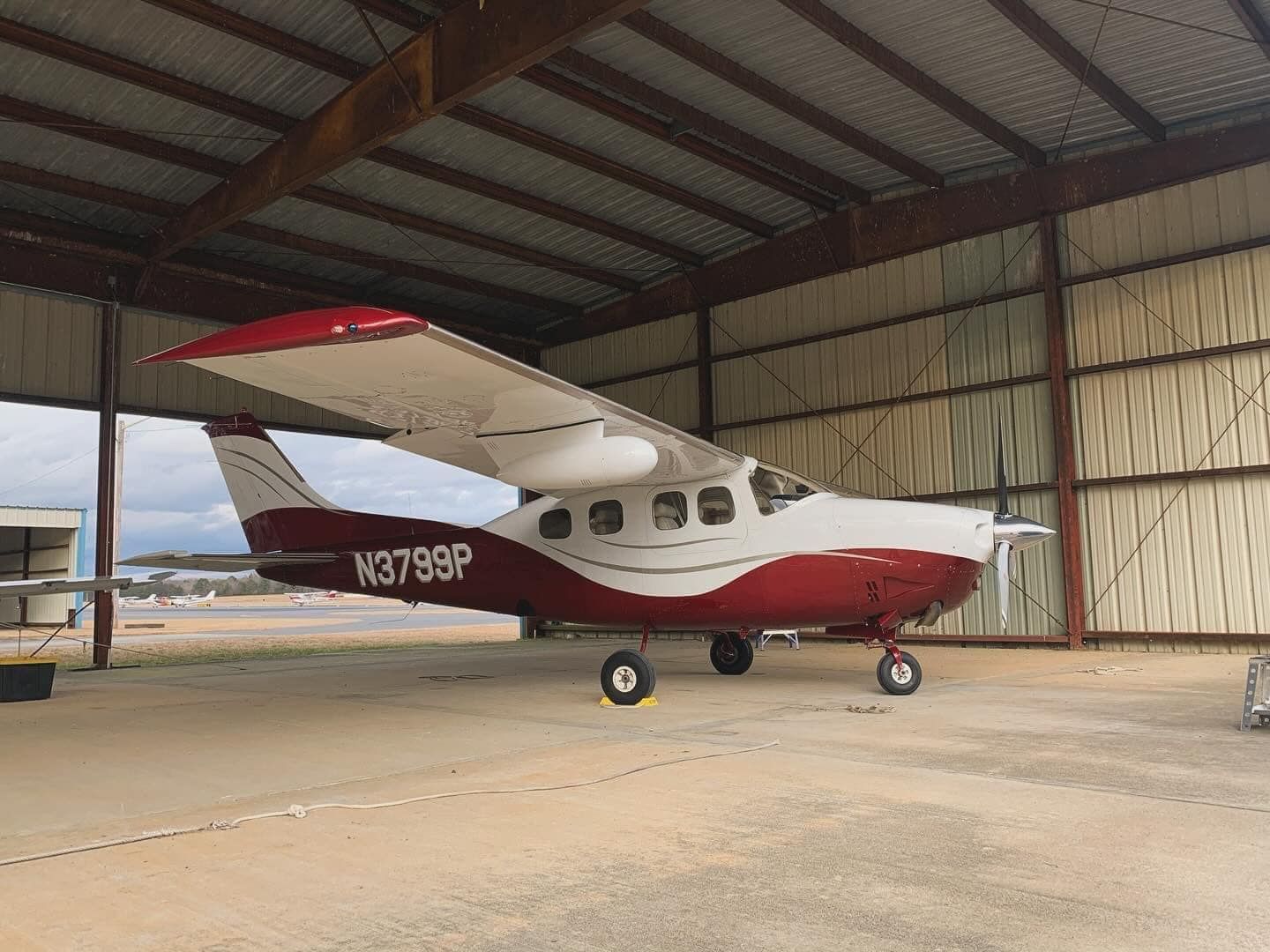 A small red and white airplane is parked in a hangar.