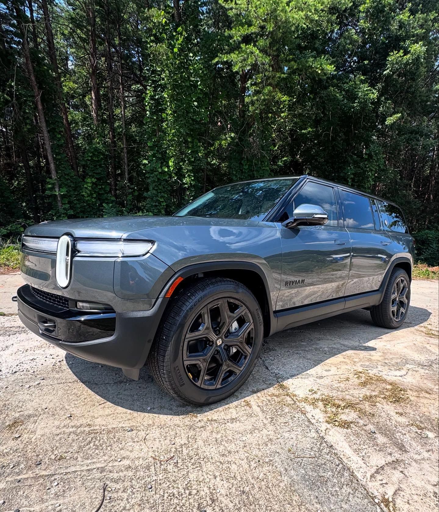 A gray suv is parked on the side of a road in front of trees.