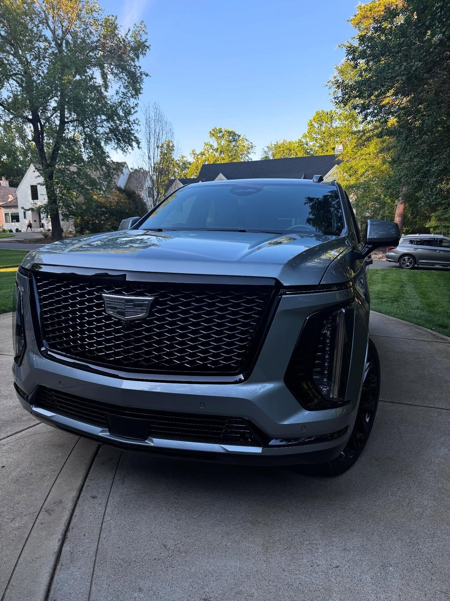 A gray cadillac escalade is parked in a driveway in front of a house.