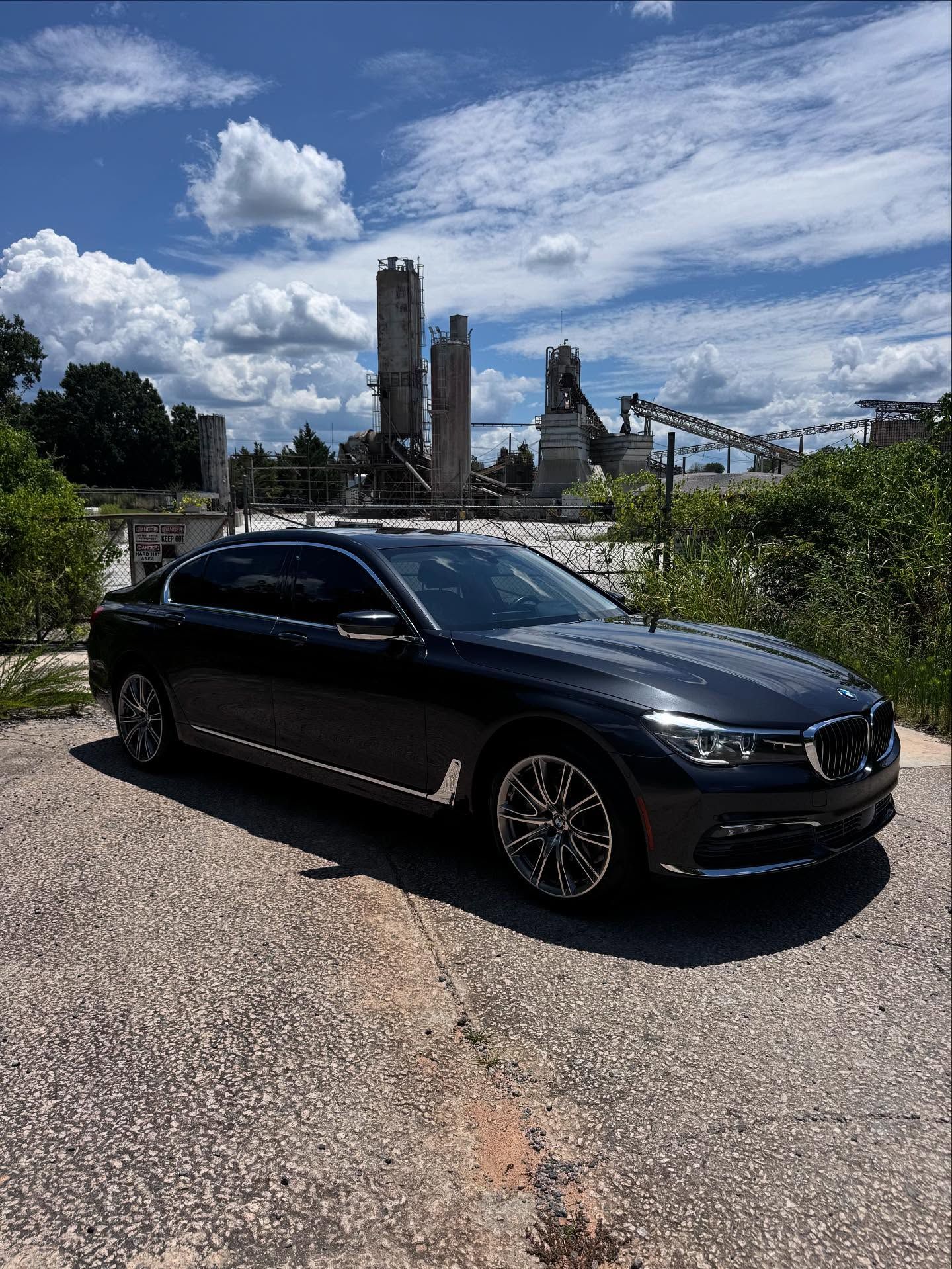 A black bmw is parked on a gravel road in front of a factory.
