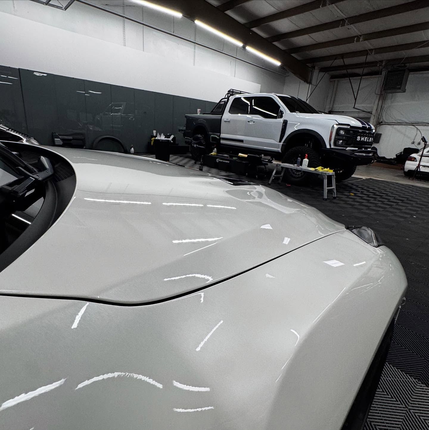 A white truck is parked next to a white car in a garage.
