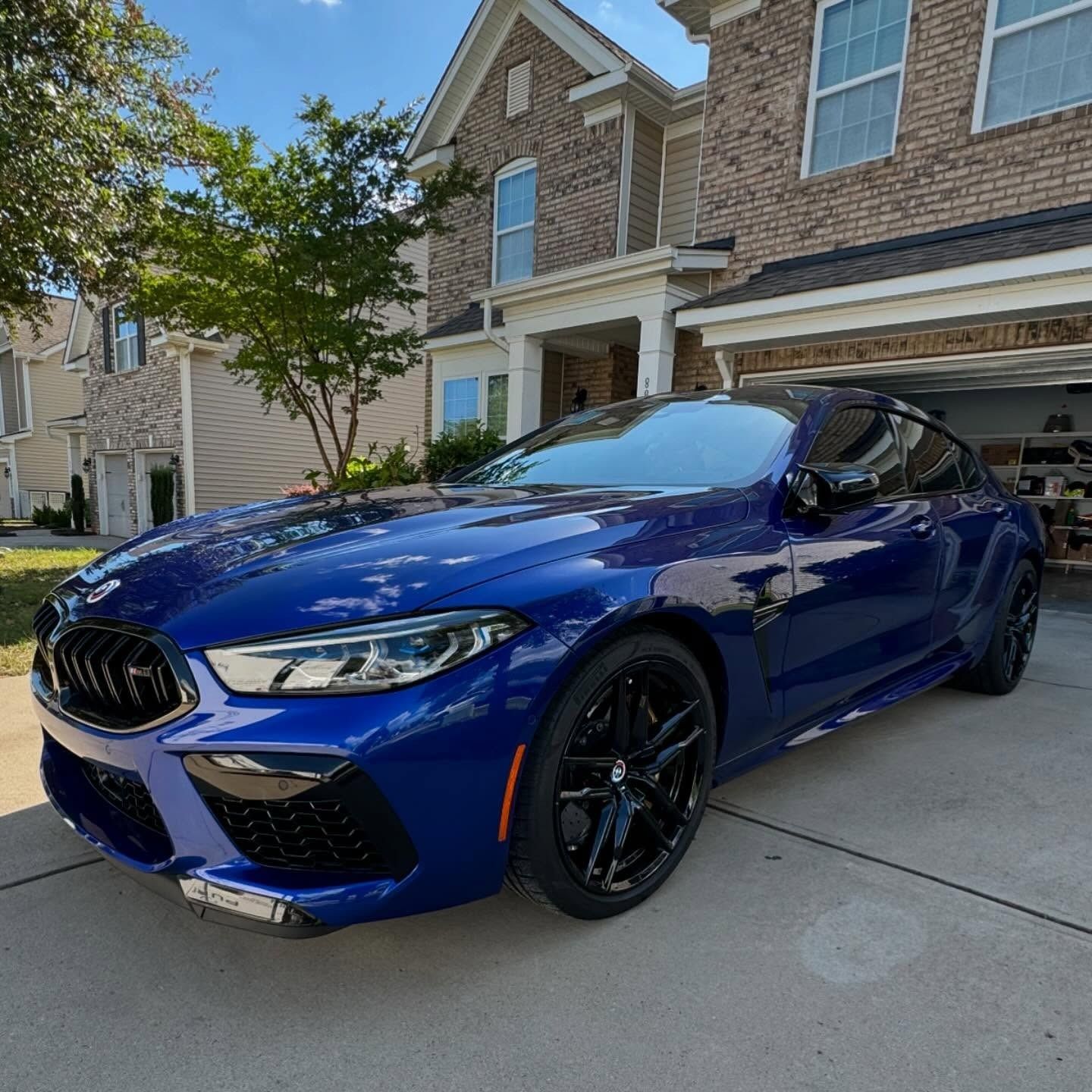 A blue sports car is parked in front of a brick house.