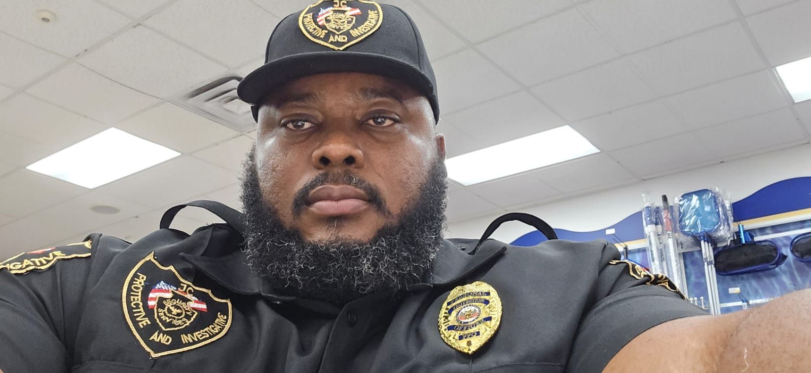 A man with a beard and a hat is wearing a security uniform.