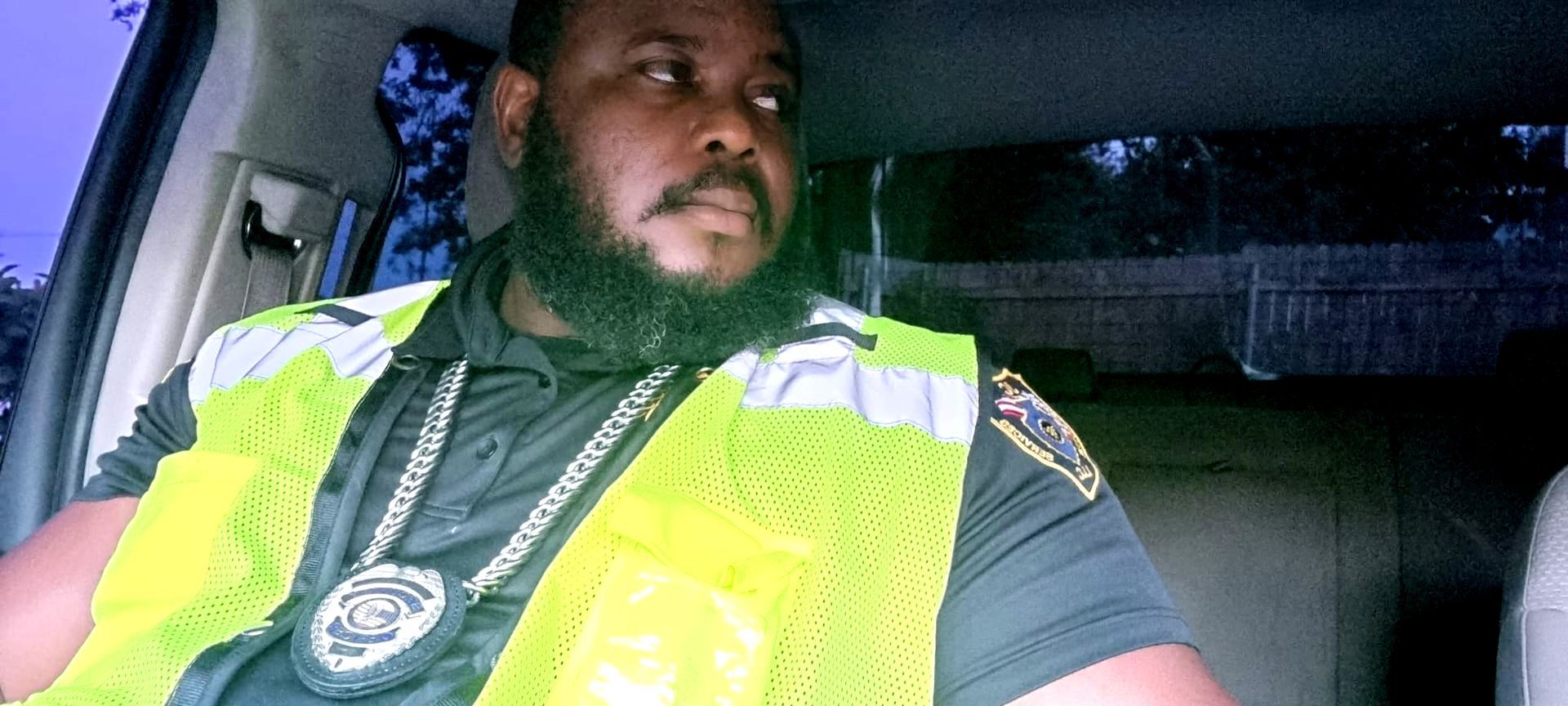 A man with a beard is sitting in a car wearing a yellow vest.