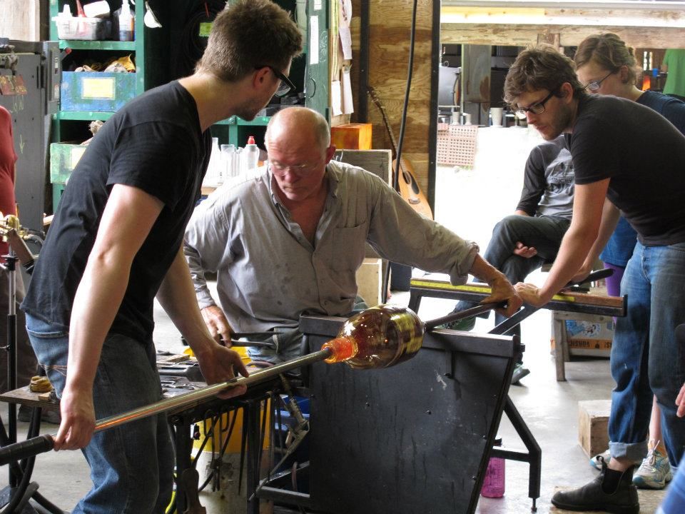 Glassblowing class; instructor guides students working with molten glass, focused activity.