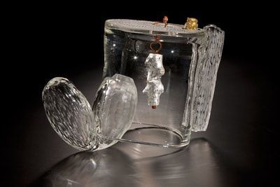 Clear glass sculpture with textured wings and a hanging silver form.