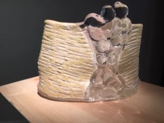 Sculpture of two figures, light-colored textured walls, with a clear torso, on a wooden surface.