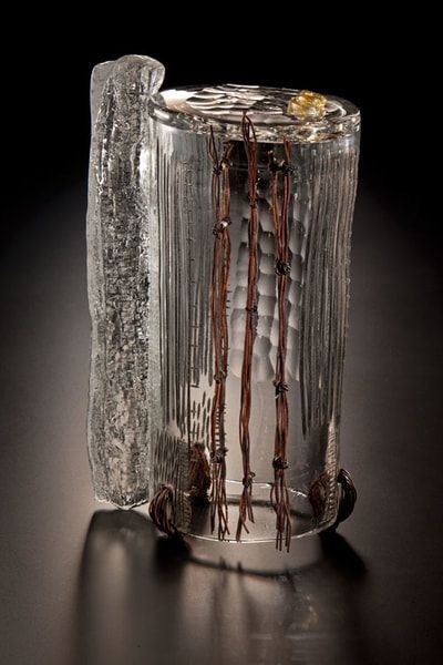 Glass sculpture with vertical, brown rods inside; rough texture on outside with ice-like piece attached.