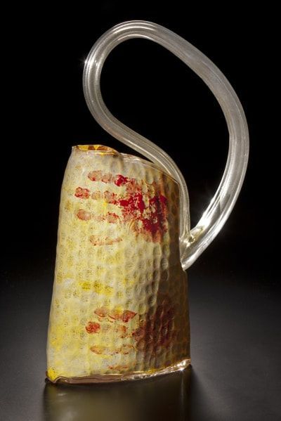 Glass art piece with yellow, red, and clear glass, featuring a curved handle and textured body.