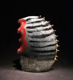 Sculpted ceramic piece: gray and black striped with red detailing, gold spines, and a ribbed base.