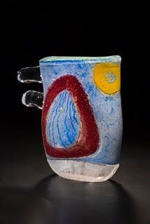 Colorful glass mug with red, blue, and yellow abstract shapes, two handles, on black background.