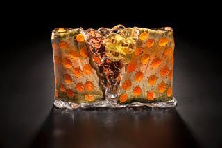 Glass art sculpture with orange polka dots and a central crack, set against a black background.