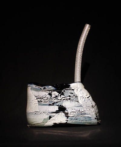 Sculptural ceramic piece; textured white and black vessel with a curved, silver tube rising.