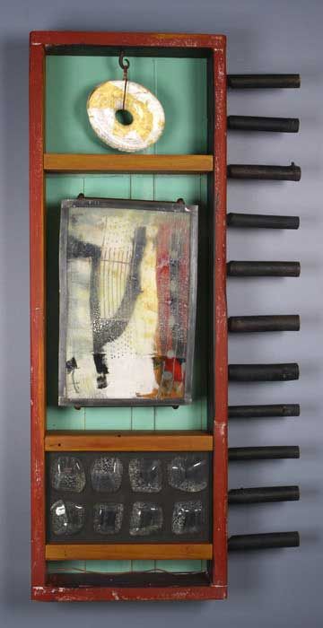 Mixed media artwork: red-framed panel with abstract painting, ceramic donut, glass squares, and black cylinders on the side.