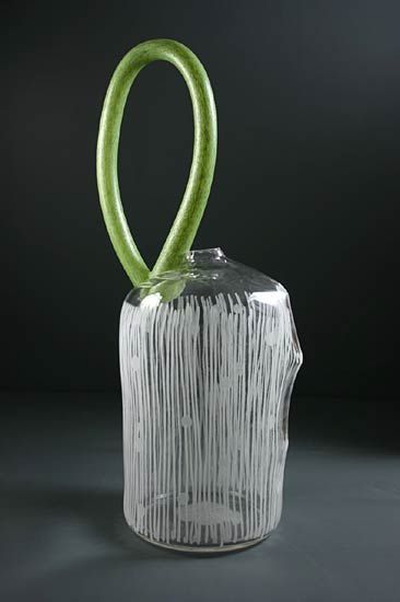 Glass vase with a green looped handle; white, vertical lines on the clear body.