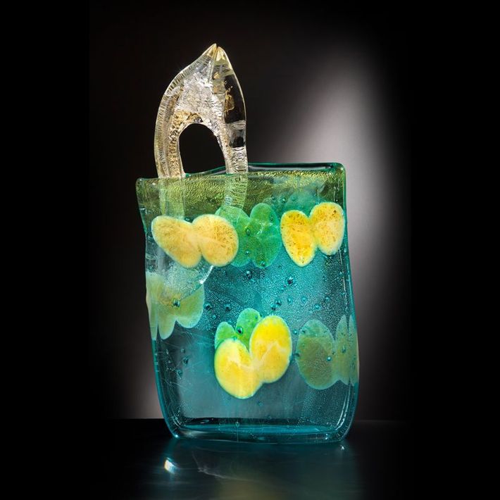 Turquoise glass vase with yellow and green floral designs, clear handle, against a black background.