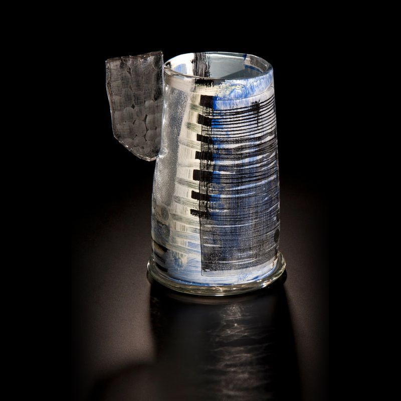 A glass vase, possibly repurposed, with a flap and layered blue and black design, sits on a black surface.