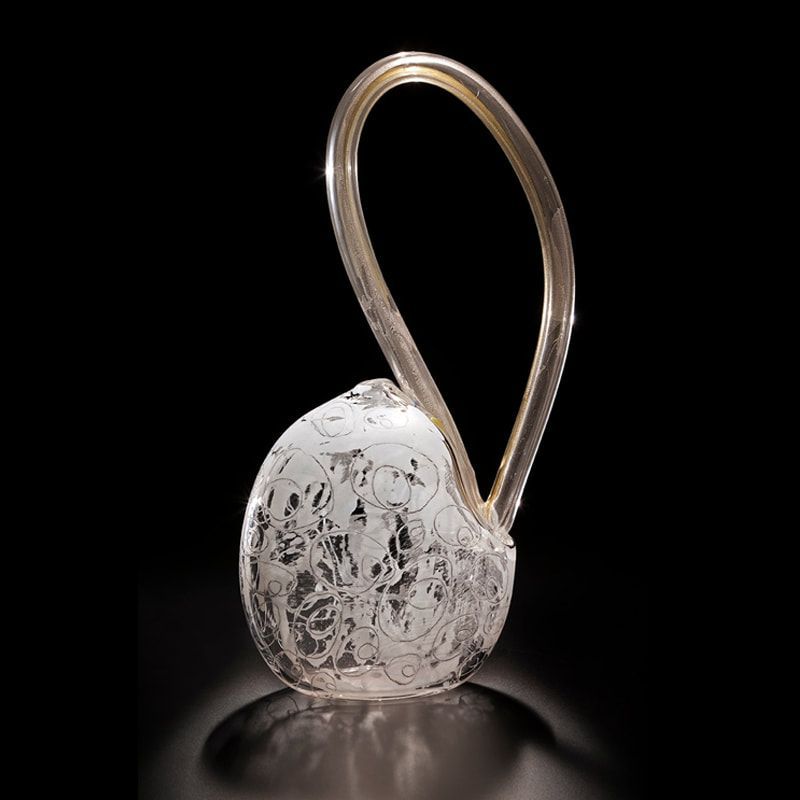 Glass sculpture with etched design and arched handle, against a black background.