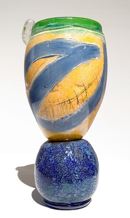 Ceramic vase with blue, yellow, and green glazes, sitting atop a smaller, speckled blue base.