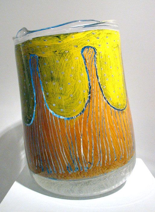 Colorful glass art, cylindrical with yellow top, dripping blue and orange streaks, clear base.