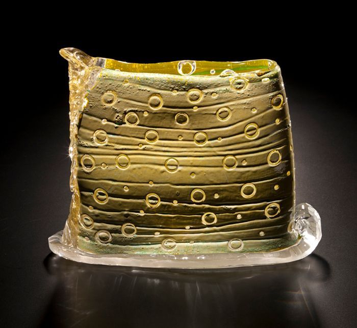 Glass sculpture, yellow-green with horizontal lines and circular bubbles, rectangular shape, sits on a clear glass base.
