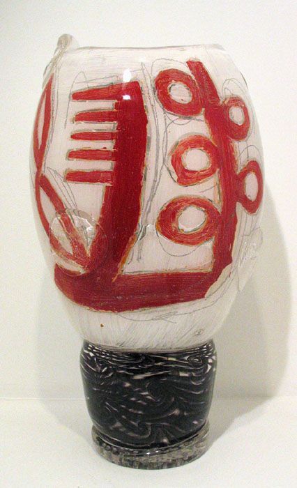 White and red abstract sculpture with hair comb and scissors on a black base.