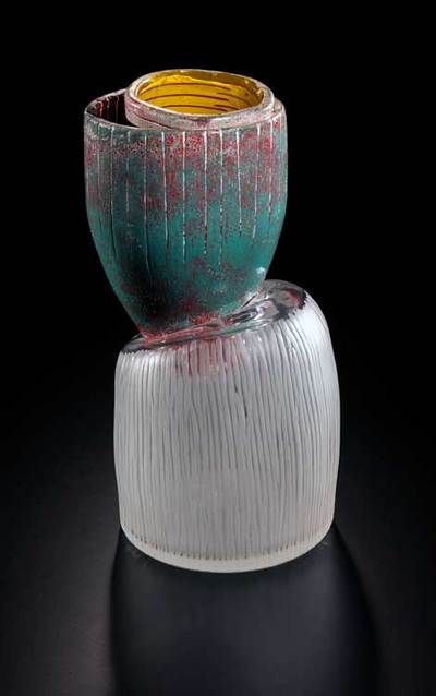 Sculptural glass vessel in emerald, silver, and yellow. The design is abstract and tilted against a black background.