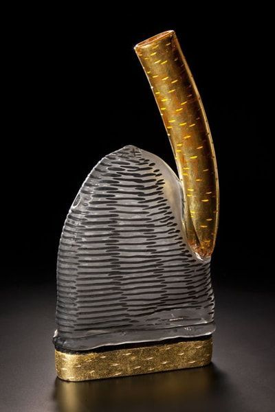 Sculptural glass art. Grey striped form, arched gold element, gold base, black background.