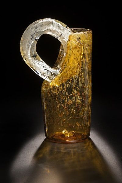 Amber glass vase with a clear, circular handle, resting against a black background.