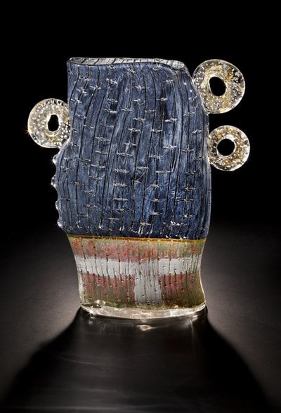 Glass sculpture of a head with blue texture and three gold circles, sitting on a red, white, and green base.