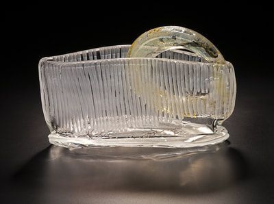 Clear glass sculpture of a textured rectangular basket with a curved handle, on a dark surface.