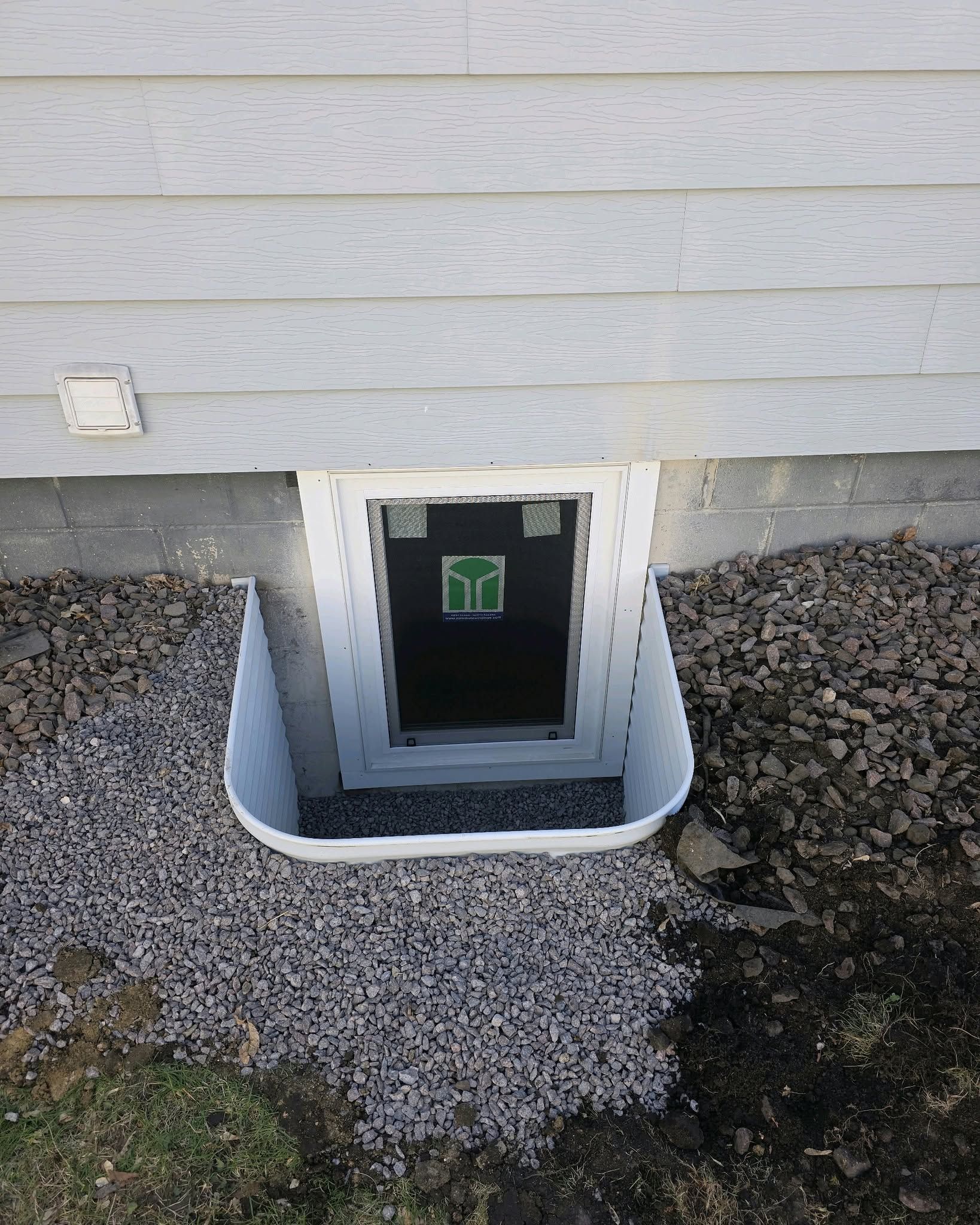 White window well with gravel and gray siding.