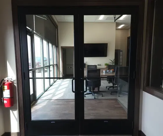Glass double doors leading into an office space with a table and chairs visible; a fire extinguisher hangs to the left.