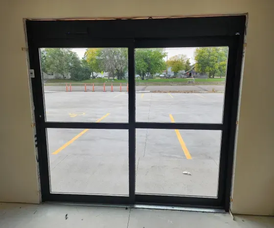 Glass sliding doors facing an empty parking lot with yellow painted lines and orange cones.